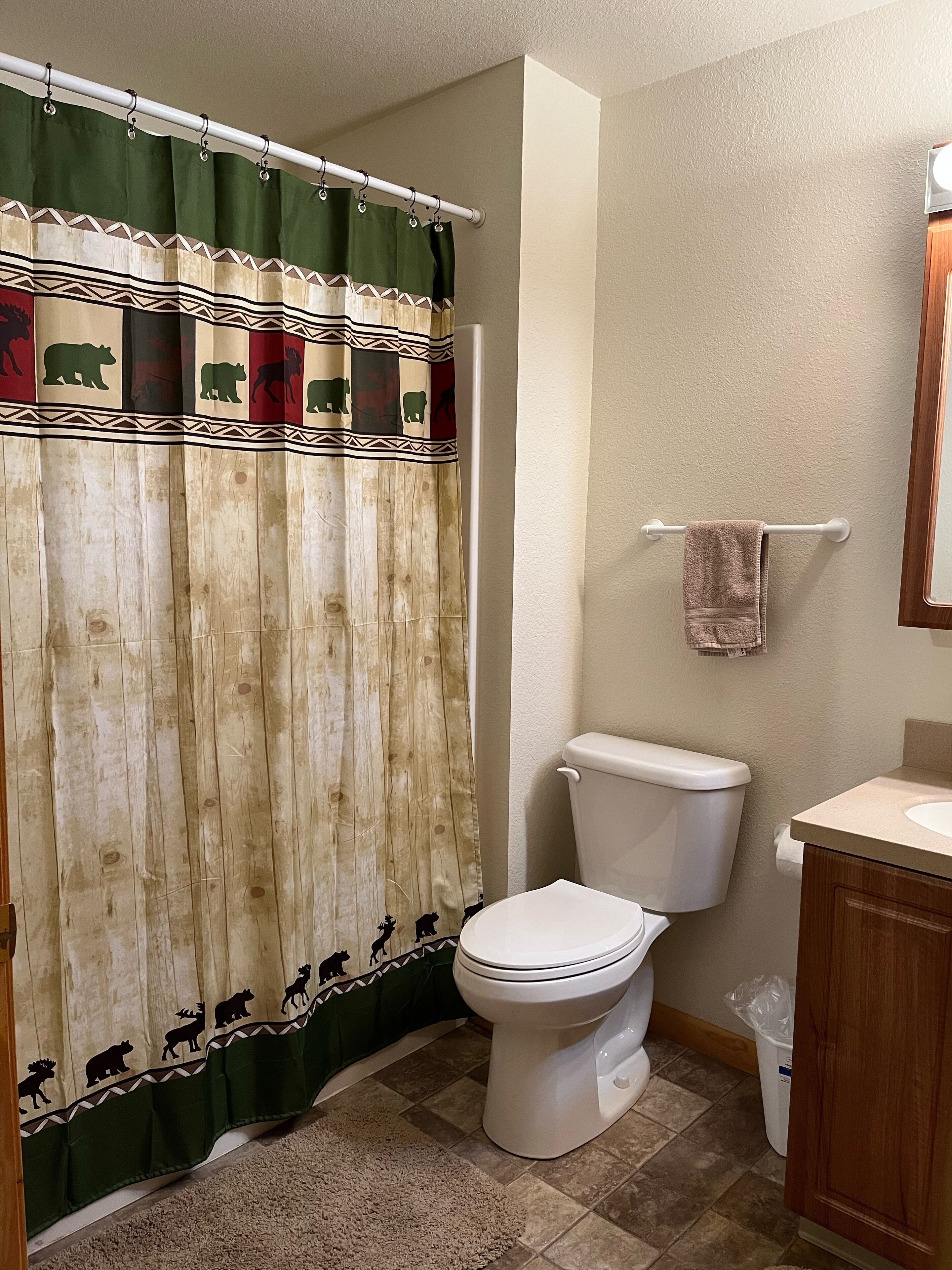 Une salle de bain équipée de toilettes, d’un lavabo, d’un porte-serviettes et d’un rideau de douche à motifs animaliers.