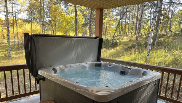 A hot tub on a covered deck with a wooden bench and steps.