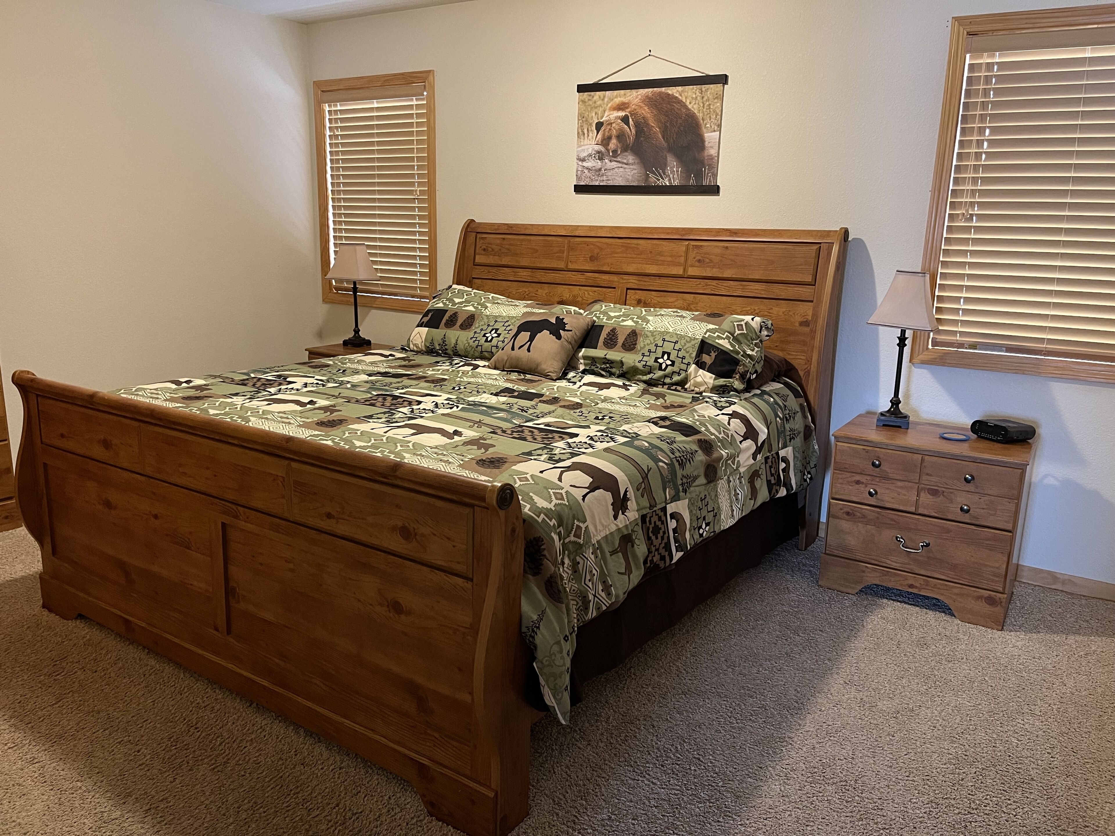 A wooden bed with a patterned bedspread, a bedside table with a lamp, and a framed picture on the wall.