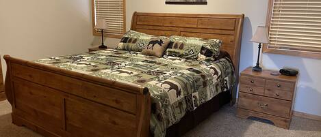 A wooden bed with a patterned bedspread, a bedside table with a lamp, and a framed picture on the wall.