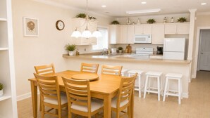 A modern kitchen with white cabinets, a central island, and a dining area with wooden chairs and stools.