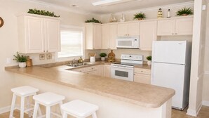 A kitchen with white cabinets, a central island with stools, a microwave, stove, and refrigerator.