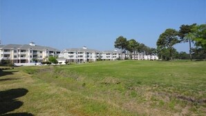 A multi-story hotel with a flat roof and balconies, surrounded by a grassy area and trees.