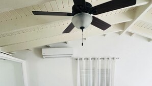 Une chambre avec un grand lit, deux tables de chevet, un ventilateur de plafond et une fenêtre avec des rideaux.