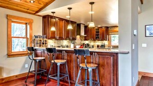 A kitchen with wooden cabinets, a bar area with stools, and pendant lighting.
