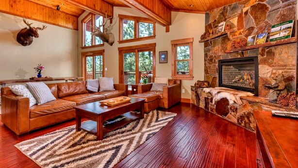 A spacious living room with a stone fireplace, leather sofas, and a mounted deer head.