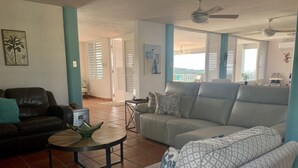 A living room with a sofa, a coffee table, and a black leather chair. There is a ceiling fan and a window with blinds. - Hacienda Margarita—Private Pool Spacious Home with VIEWS! (Luquillo)