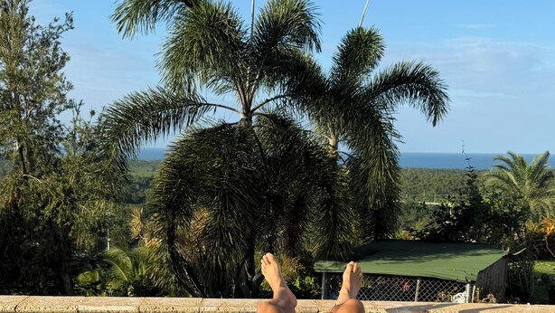 A person relaxing on a pool float in a clear pool with a view of palm trees and a distant landscape. - Hacienda Margarita—Private Pool Spacious Home with VIEWS! (Luquillo)