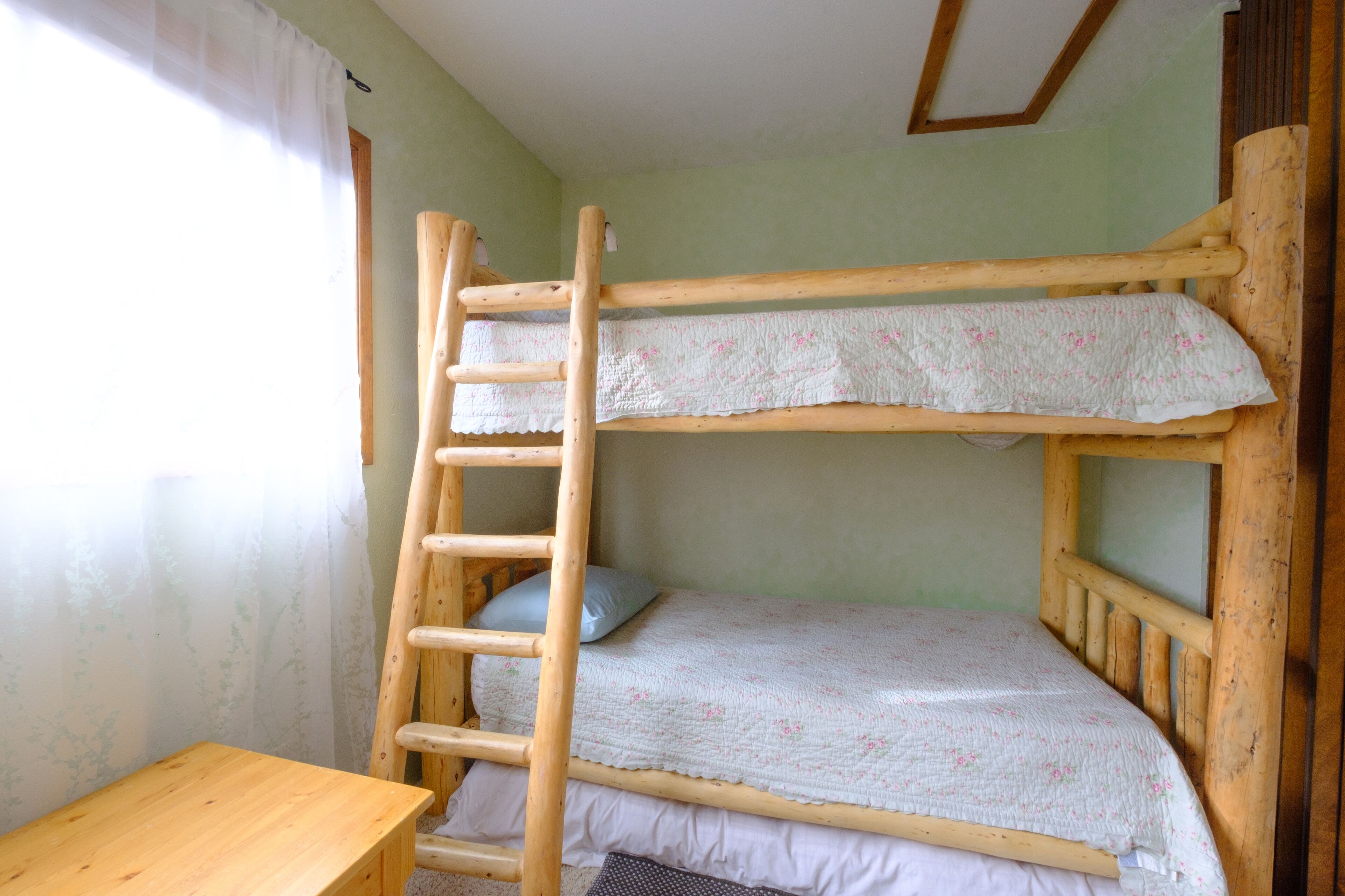 Un letto a castello con una scala in legno, un tavolino di legno e una finestra con tenda.