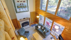 Un interior cálido de cabaña con chimenea, ventanas amplias y vistas al exterior.