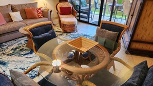 A living room with a glass coffee table surrounded by wicker chairs, a sofa, and a patterned rug. - BEAUTIFUL POIPU OCEAN VIEW 2 BRD 2.5 BATH Condo with A/C 
Great Fall Rates!
 (Koloa)