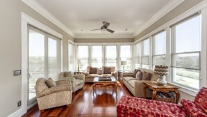 A spacious living room with hardwood flooring, large windows, and a ceiling fan. - Spacious, Updated Home, Ocean Views, Pool, Elevator, Walk to Beach & Restaurants (Isle of Palms)