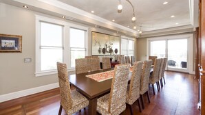 A dining room with a large table and wicker chairs, large windows, and a chandelier. - Spacious, Updated Home, Ocean Views, Pool, Elevator, Walk to Beach & Restaurants (Isle of Palms)