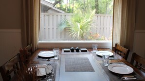 Mesa de jantar posta para quatro com jogos americanos, pratos e copos.