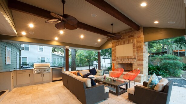 Cocina exterior con parrilla, zona de estar con sofás y sillones, y chimenea de piedra.