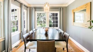 Un comedor con una mesa larga, sillas, un candelabro y ventanas amplias.