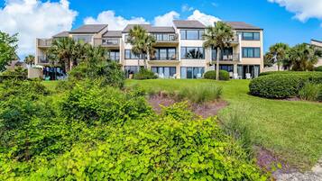 A multi-story residential building with balconies, surrounded by lush greenery and palm trees.