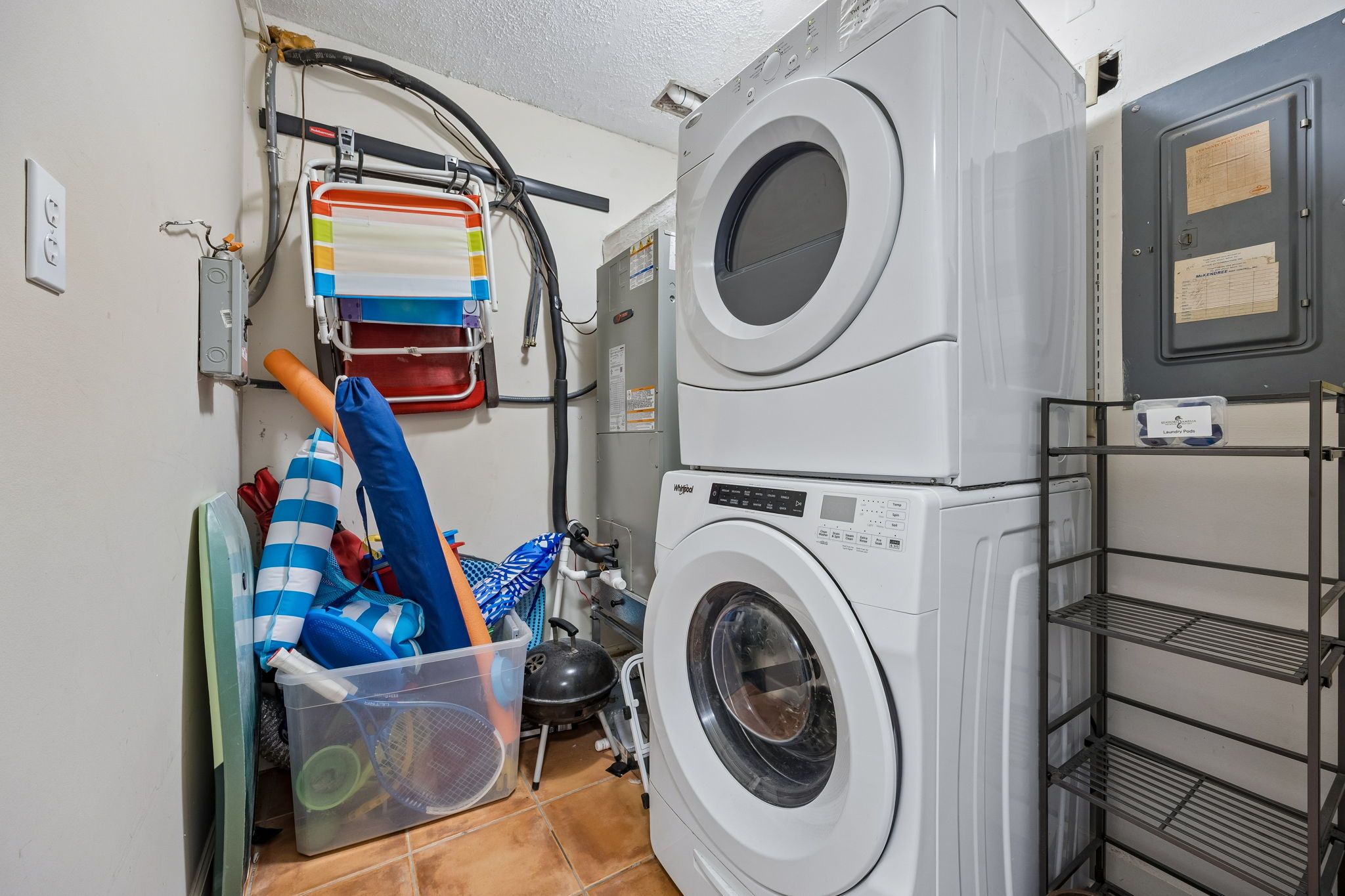 Een wasserette met twee gestapelde wasmachines, een droogrek en een plastic bak met diverse spullen.