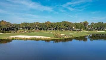Un campo de golf con un estanque, árboles y edificios al fondo.