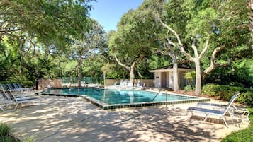 Piscina con sillas de descanso y un pequeño edificio, rodeado de árboles.
