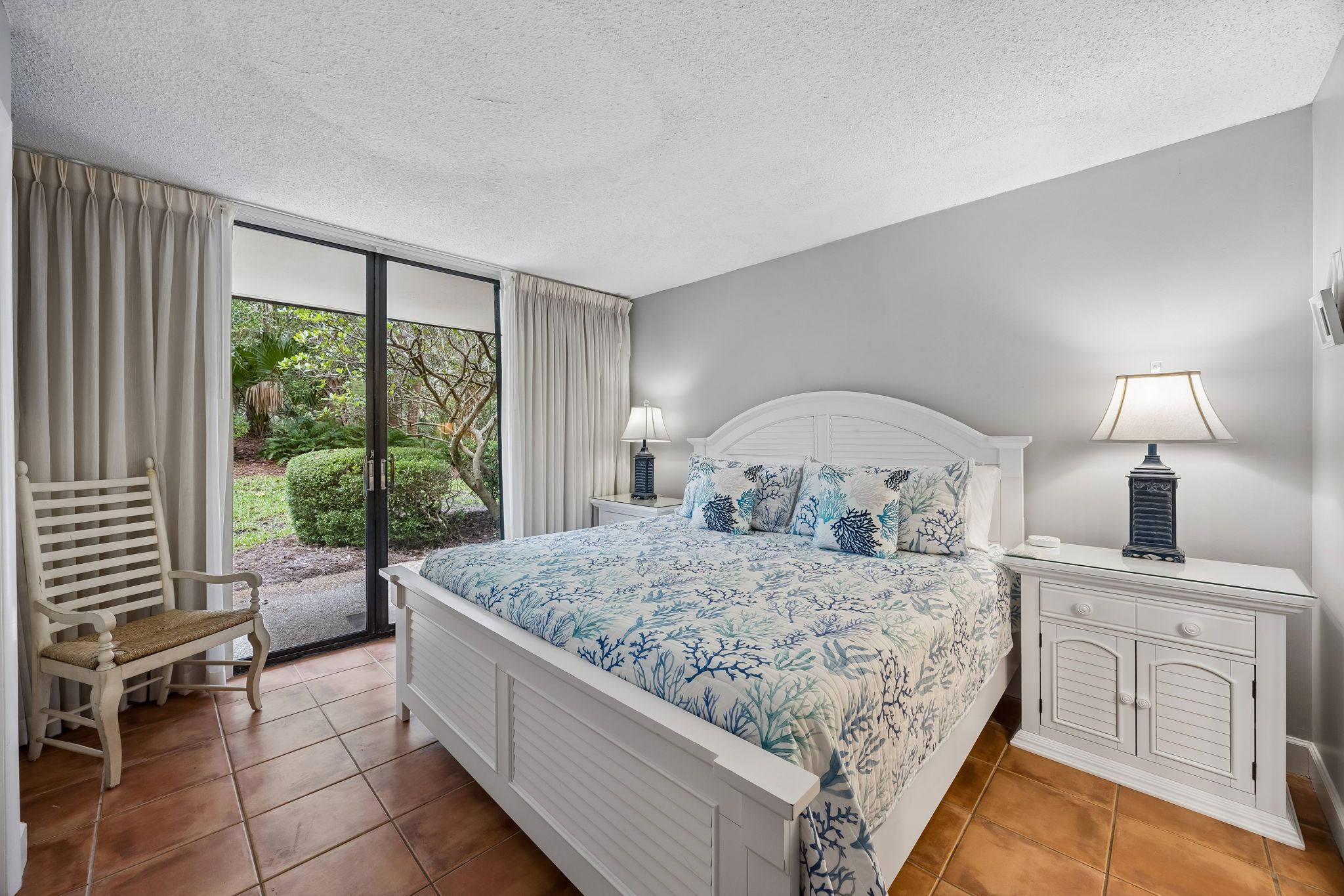 Un dormitorio con cama, mesita de noche, una silla y vistas al exterior.