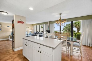 A spacious living area with a large island, a dining table with chairs, and a view of the outdoors.