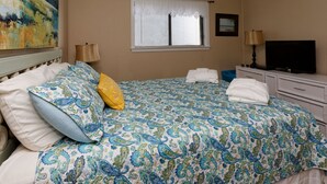A bedroom with a bed, pillows, a window with blinds, a television, and a painting on the wall. - Beach Resort, Walk to the Ocean, Free Secure Wi-Fi in Building 1 (Hilton Head Island)