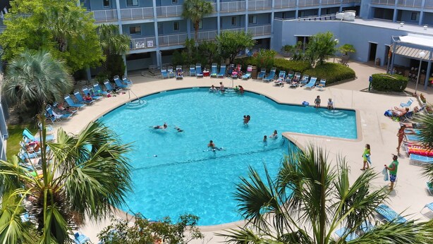 A large pool surrounded by lounge chairs and palm trees, with a multi-story building in the background. - Beach Resort, Walk to the Ocean, Free Secure Wi-Fi in Building 1 (Hilton Head Island)