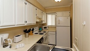 A compact kitchen with white cabinets, a stove, a microwave, a refrigerator, and a sink with a dish rack. - Beach Resort, Walk to the Ocean, Free Secure Wi-Fi in Building 1 (Hilton Head Island)