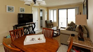 A living room with a wooden dining table, chairs, a sofa, a TV, and a lamp. - Beach Resort, Walk to the Ocean, Free Secure Wi-Fi in Building 1 (Hilton Head Island)
