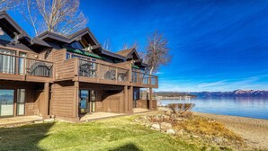 A wooden cabin with a balcony overlooking a lake and mountains.