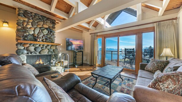 A spacious living room with a stone fireplace, leather sofas, a flat-screen TV, and a balcony with a scenic view.