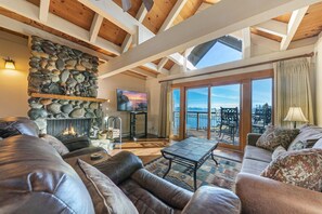 Un salón amplio con chimenea de piedra, sofás de cuero, un televisor de pantalla plana y un balcón con vistas panorámicas.