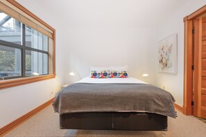 Een slaapkamer met een bed, een raam, een deur en een aan de muur hangend kunstwerk.