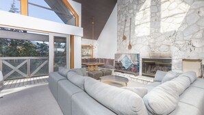 Ein modernes Wohnzimmer mit Kamin aus Stein, einem großen, grauen Ecksofa und einem Essbereich mit Holztisch und -stühlen.
