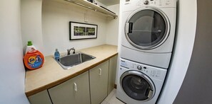 Een wasruimte met een wasmachine, een wasbak en een fles Tide wasmiddel.