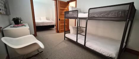 Een stapelbed met bureau en stoel, een nachtkastje met boeken, en een deur die naar een inloopkast leidt.