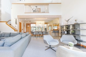 A spacious living area with a large grey sofa, a dining table with chairs, a staircase, and a modern chandelier. - Pinnacle Ridge 6 - Ski in Ski out, Private Hot Tub, Wood Fireplace (Whistler)