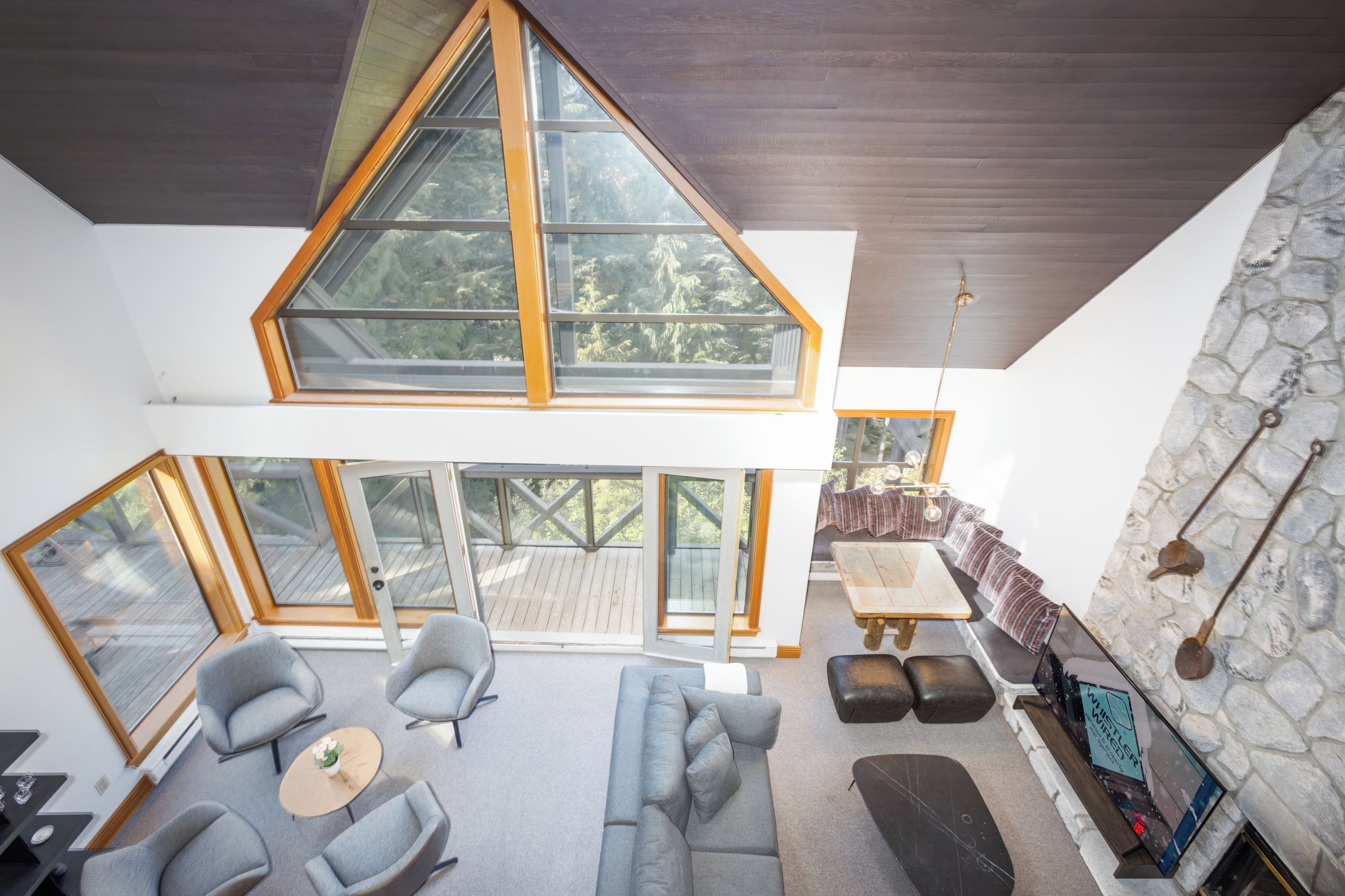A modern interior with a loft-style ceiling, large windows, a stone fireplace, and a cozy seating area.