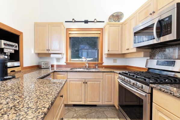 A kitchen with granite countertops, wooden cabinets, a stainless steel stove, a microwave, and a window with blinds.