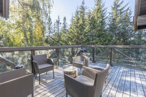 An outdoor deck with wooden flooring, surrounded by glass railings, featuring two sofas and a round table.