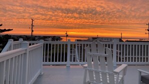 A white wooden deck with a white railing, overlooking a sunset over a body of water.