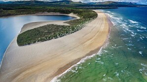 Vista aérea de un paisaje costero con una playa arenosa, aguas azules cristalinas y una pequeña isla con vegetación.