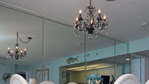 A dining area with white upholstered chairs, a glass table, and a chandelier.