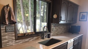 A kitchen with a double sink, a dishwasher, and a window with a view of trees. - T.P.'S Place on the Stunning Aqua Blue Waters of Torch Lake (Bellaire)