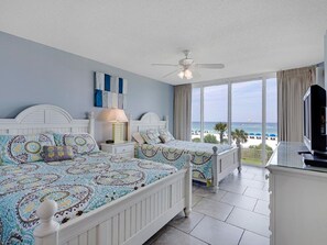Enjoy stunning ocean views from the large window, featuring two comfortable beds and a TV on a stand.