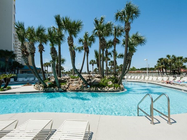 Relax by the pool surrounded by palm trees and a small rocky island.