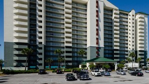 Un hotel grande con varios pisos, una entrada principal y un estacionamiento con varios automóviles.