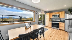 A modern kitchen with wooden cabinets, a stainless steel refrigerator, and a large window overlooking a scenic landscape.