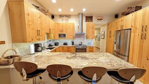 Una cocina con armarios de madera, una isla central con taburetes de bar, un refrigerador de acero inoxidable y un microondas.
